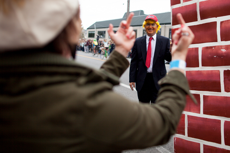 Wearing the infamous red cap and tie, a performer imitating Trump and carrying a big brick wall provokes a reaction from an onlooker.