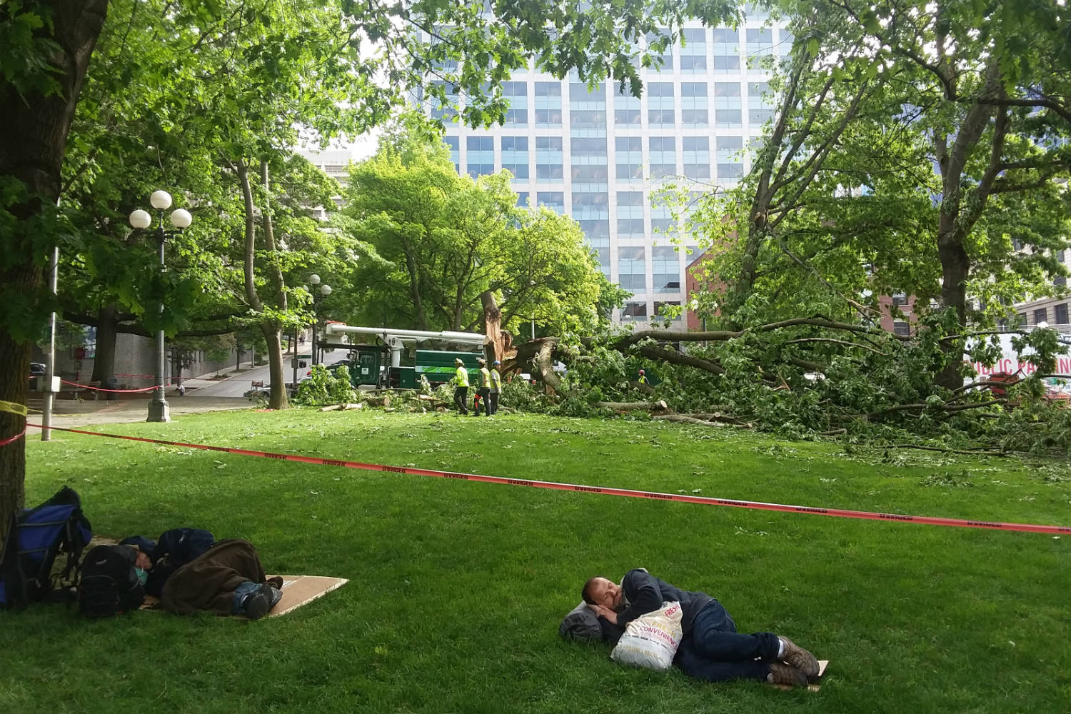 A homeless person sleeps in City Hall Park in front of work crews. Photo by Casey Jaywork
