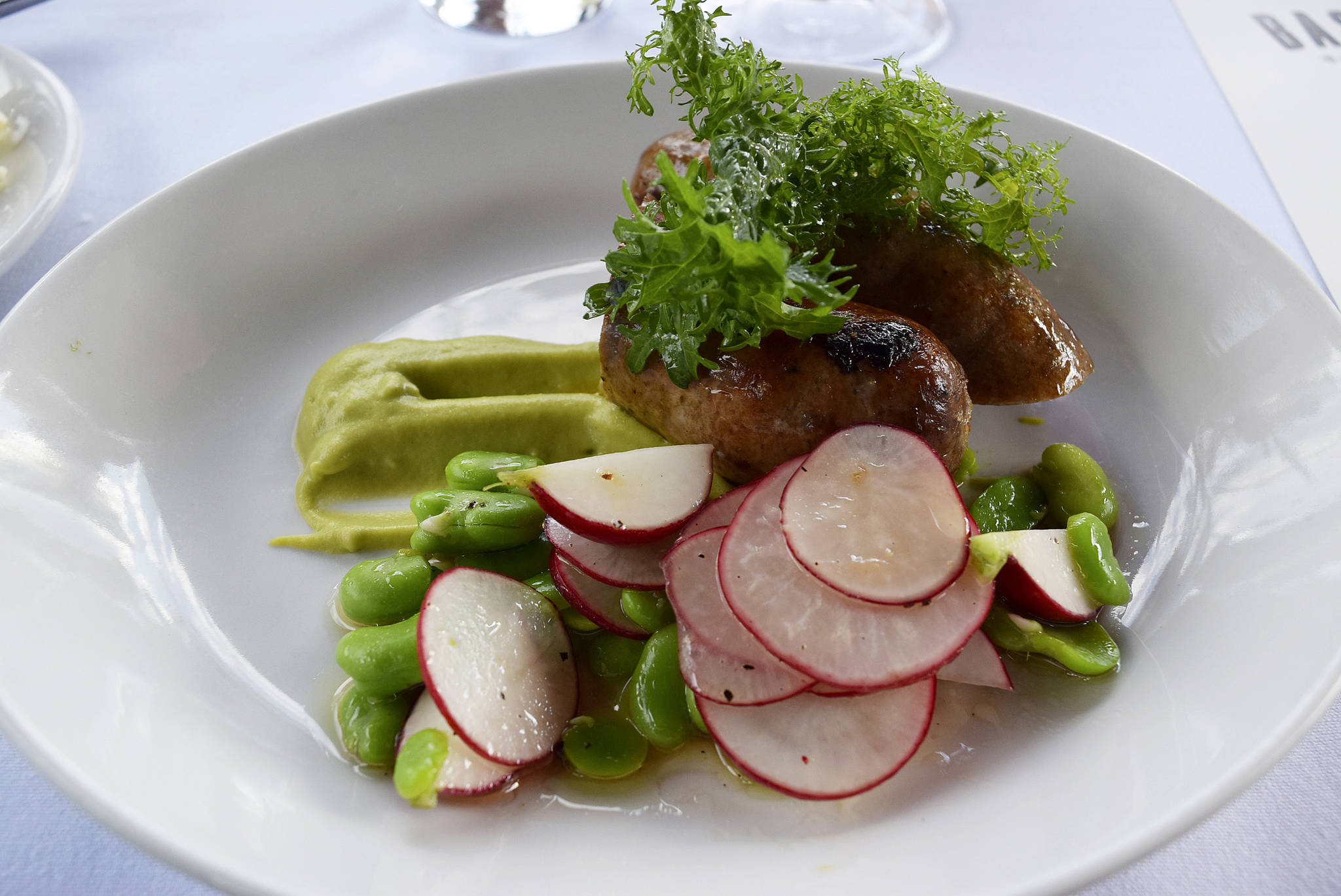 Grilled lamb sausage with fava bean, frilly greens, and 
marinated radishes from a Bastille Rooftop Garden Dinner. 
Photo courtesy Bastille Café & Bar