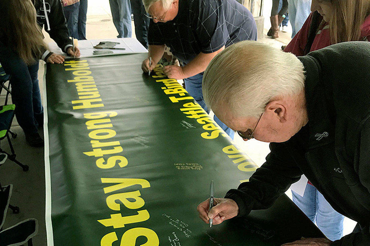 Bruce McDonald, foreground, and his 15-year-old daughter, Chloe, join others outside the accesso ShoWare Center on Saturday in signing a banner supporting the Humboldt, Saskatchewan junior hockey team. MARK KLAAS, Kent Reporter
