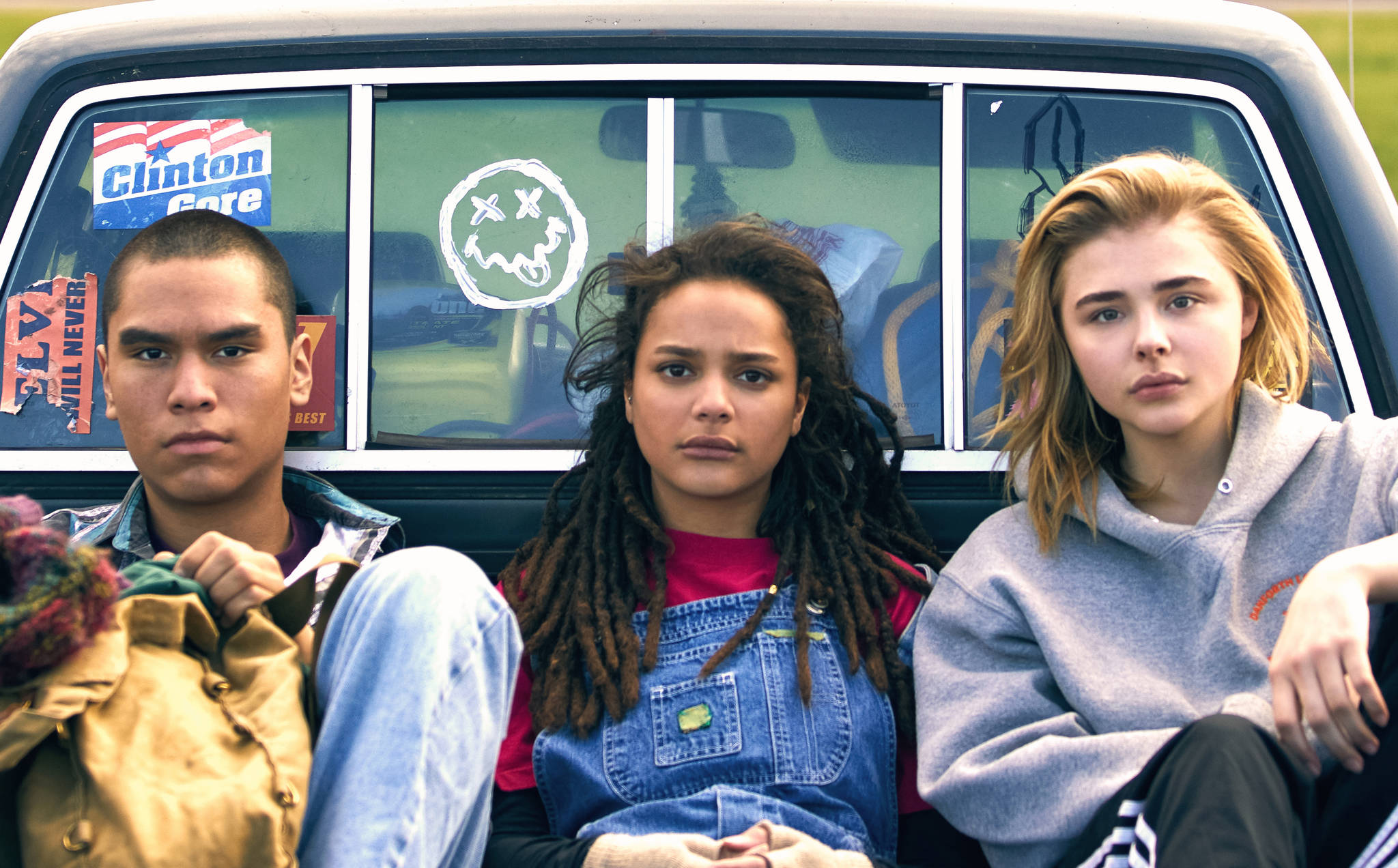 Image from the film The Miseducation of Cameron Post. Three teenagers, one boy and two girls, sit side by side in the back of a truck. They all look directly at the camera.