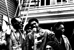 Bobby Seale speaks at a Free Huey rally in DeFremery Park. At left is Black Panther Party Captain Bill Brent; at right is Black Panther Party Captain Wilford Holliday (known as “Captain Crutch”). Oakland, Calif., 1968