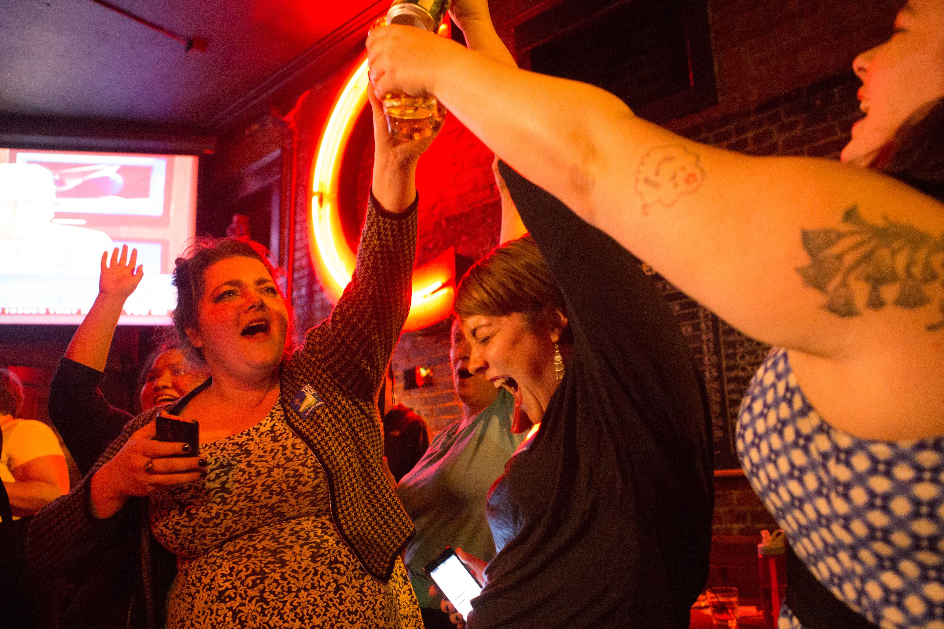 Alex Hudson (left), celebrates with attendees of the election night party at The Comet Tavern as news comes in that Prop 1 has passed.