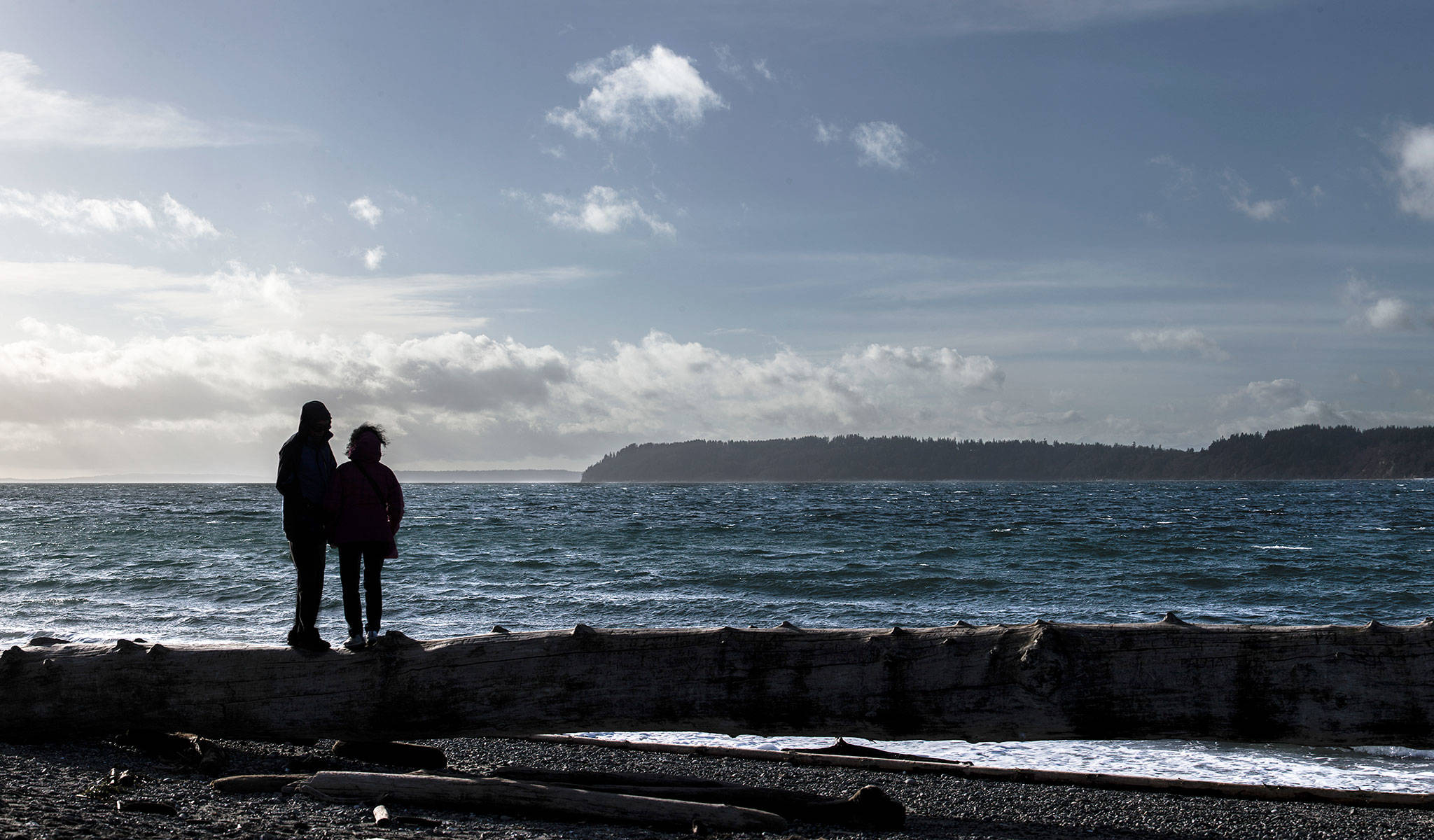 A couple stands on driftwood at the beach near Mukilteo Lighthouse Park in 2018. (Olivia Vanni / Herald file)