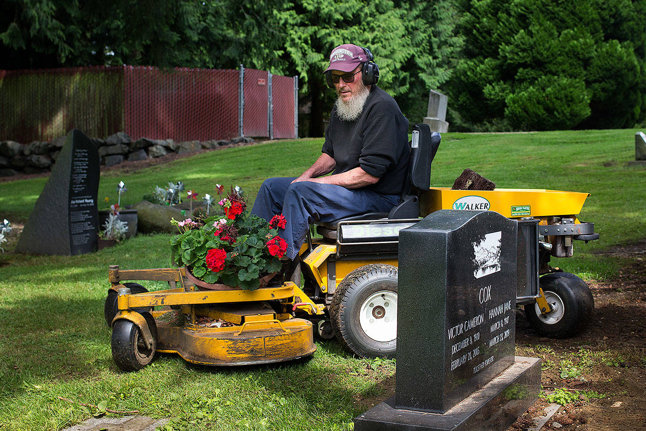 Cliff Edwards, 65, the sexton at Edmonds Memorial Cemetery & Columbarium, picks up and carries memorial flowers on his mower as he cuts the grass around headstones on Monday, Aug. 19, 2019 in Edmonds, Wash. (Andy Bronson / The Herald)