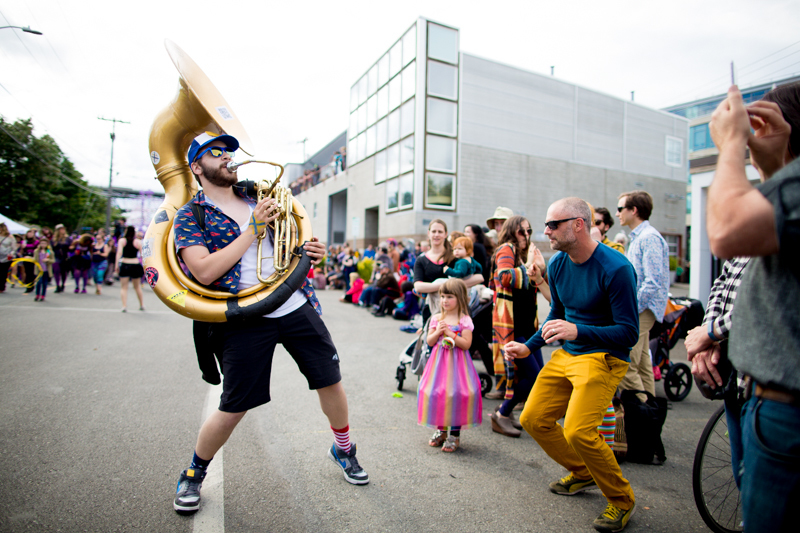 Susaphone player Logan Pendergrass with the Ten Man Brass Band dances along with a man in the street.
