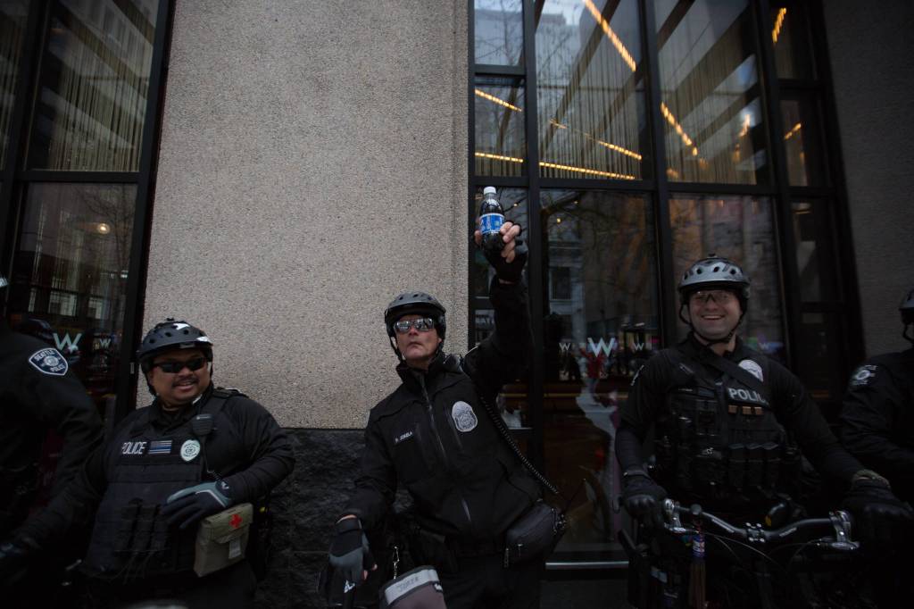 Officer Jokela of the Seattle Police Department holds up a bottle of Pepsi as protesters with the Tax March stream down Fourth Avenue towards Seattle Center, a spoof of the much maligned Pepsi ad featuring protesters giving police a soda to make peace.