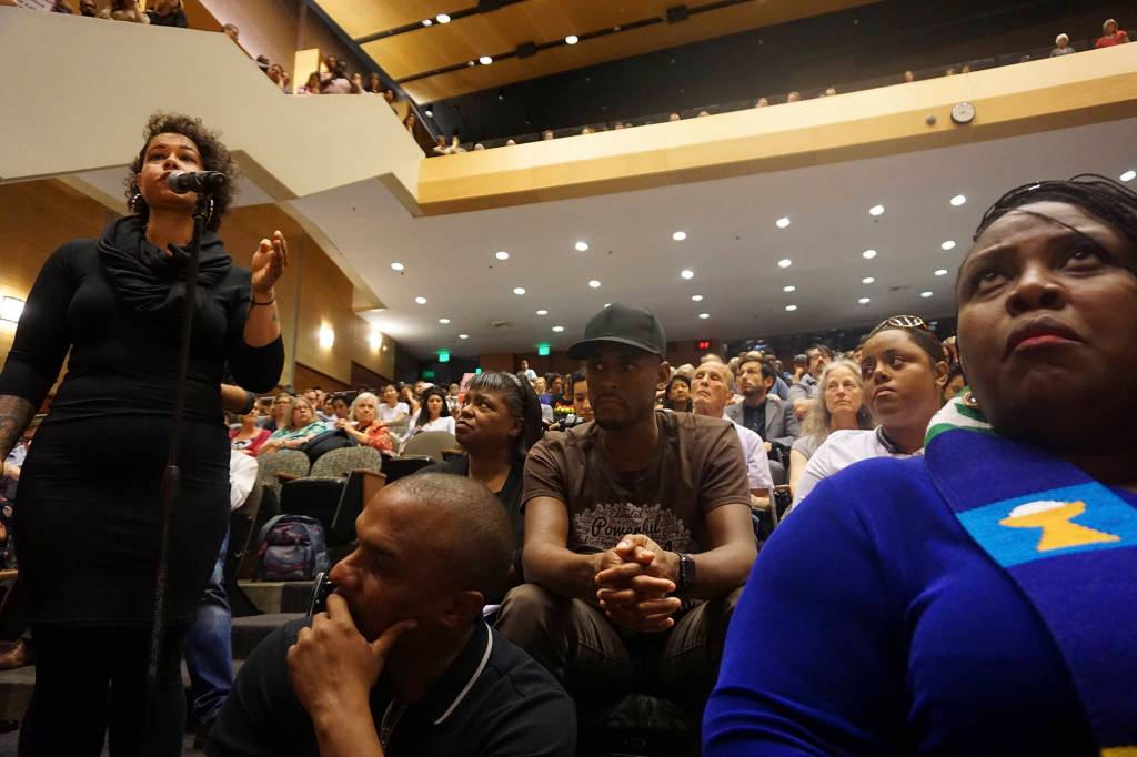 Nikkita Oliver, left, addresses the council during the June 27 hearing on the police killing of Charleena Lyles. Rev. Brown, right in blue, opened the hearing with a prayer in which she asked God to &ldquo;make us hear each other. Make us hear the things that we say, and the things that we do not say…We have permission to be angry,&rdquo; she added. &ldquo;And let us call our anger righteous, for it is such.&rdquo; Photo by Casey Jaywork
