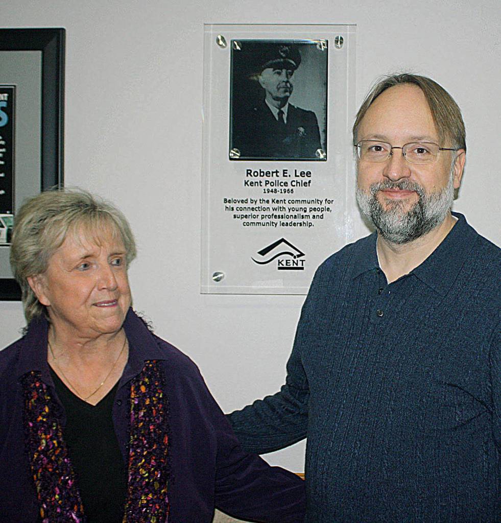 Vicki Schmitz, daughter of former Kent Police Chief Robert E. Lee, and Dietrich Schmitz, grandson of Lee, pose next to a photo of Lee at the police station lobby. Photo by Steve Hunter