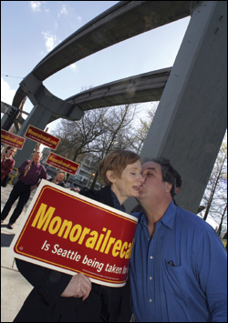 Pat Stambor (left), co-chair of the new Monorail Recall group, gets a playful peck from Dick Falkenbury, the original monorail advocate, who happened upon a protest last week.