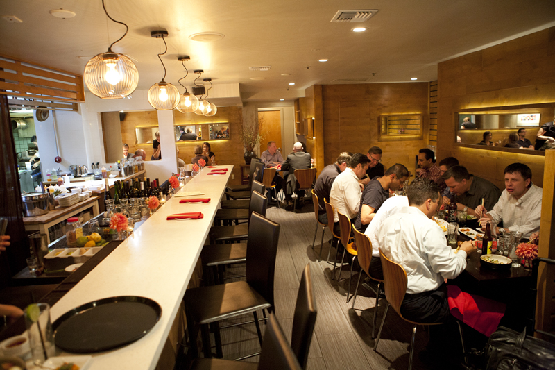 Furnished with slatted wooden walls and willow branches wriggling out of squat ceramic vases, the ell-shaped dining room hugs an open kitchen that doubles as the bar.