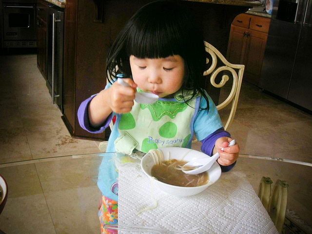 Aimee eating pho:  One of the best things about eating a bowl of pho is savoring its aroma. Aimee, my two-year-old niece, knows (or should I say, nose?) this. If I could describe her expression in this photo in one word, it would be bliss. Aimee apparently loved the fragrant and rich pho broth so much, she used two spoons to scoop it up!  Submitted by Cindy Che