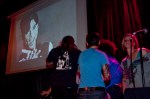 People dance on stage as Prince serenades them from the screen.