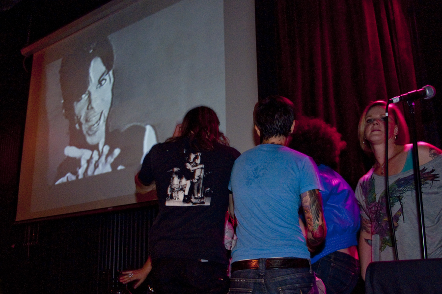 People dance on stage as Prince serenades them from the screen.