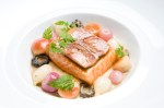 A hunk of ivory-fleshed salmon crowned with a slice of foie gras is sunk in a shallow bowl, tightly surrounded by pearl onions and mushrooms.