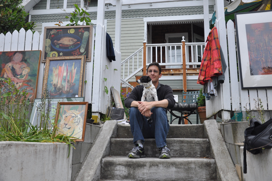A man and his dog sell paintings and other knick knacks.