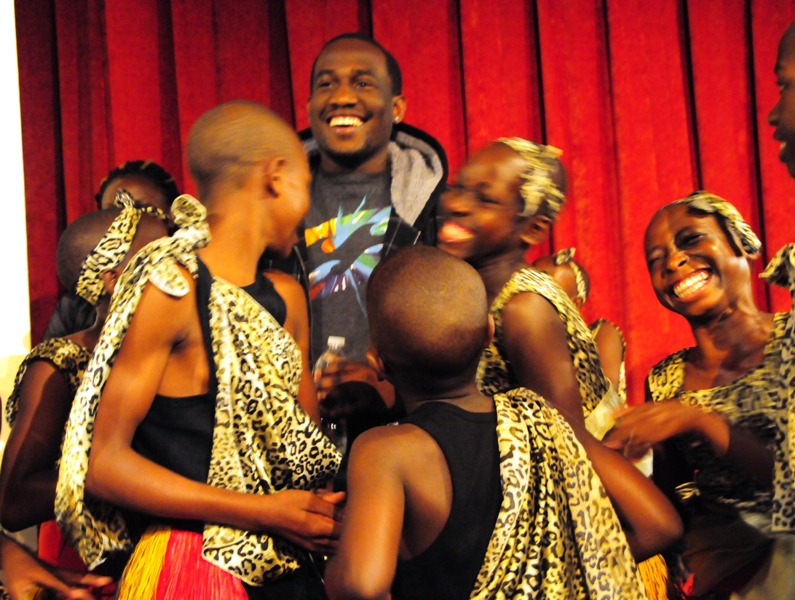 The children gather around a Uganda native who took part in Langston Hughes' youth programs when he was a teenager.