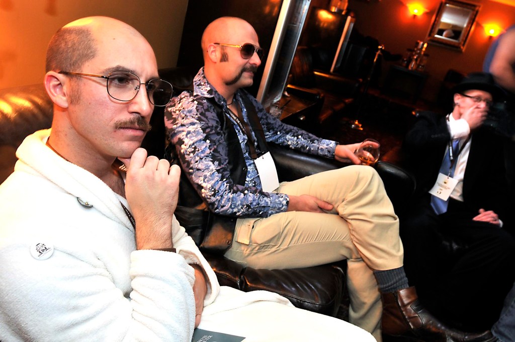 Playing the character Tobias from the show Arrested Development, Jeremy Malik of San Diego, Calif., left, Ken Schafer of Seattle, and Matt Strauch of Auburn, wait for the judging to begin during the 2010 Movember Seattle Gala Parte at Trinity on Saturday evening Nov. 27, 2010, in Pioneer Square of Seattle. Malik says this his second year participating in the fundraising event. Movember is a charity event that originated in Australia in 2003 and is growing exponentially throughout the world. As part of the fundraising challenge, men grow a mustache beginning November 1st to help raise funds for prostate and testicular cancer research. The funds go to the Livestrong Foundation and also for prostate cancer research.