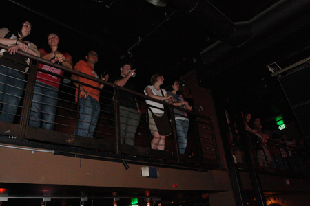 The 21+ crowd looks on from the balcony, drinks in hand.
