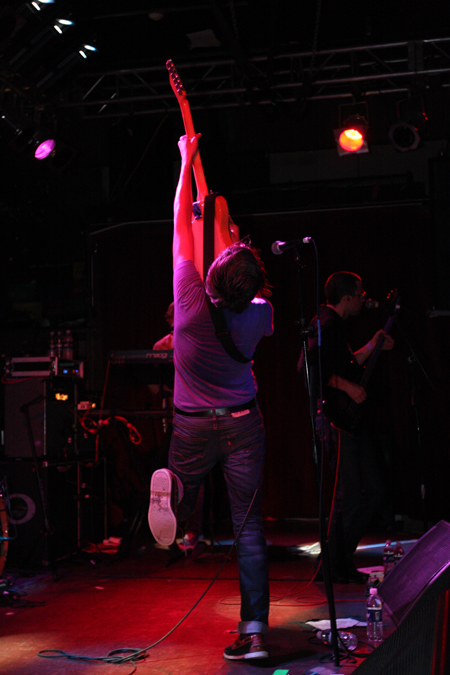 In a fitting rock pose, We Are Scientists' lead singer/guitarist raises his guitar above his head.