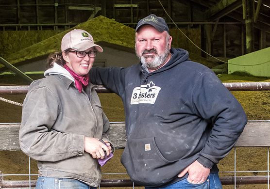 Standing on a dirt path, alongside a neat stack of irrigation pipes,