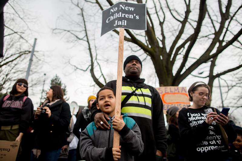 A young boy holds up a sign protesting the planned expansion and renovation of the King Couty Youth Detention Center.