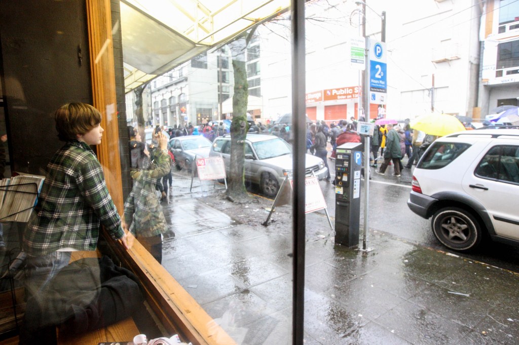 A young boy watches protesters through the window of the Northwest Film Forum theater, Saturday. Protesters of the Walking While Black: Always Dangerous Until Proven Otherwise protest marched around Capitol Hill for William Wingate's incident in which a Seattle police officer arrested Wingate claiming the golf club he used as a cane was a weapon on July 9, 2014.