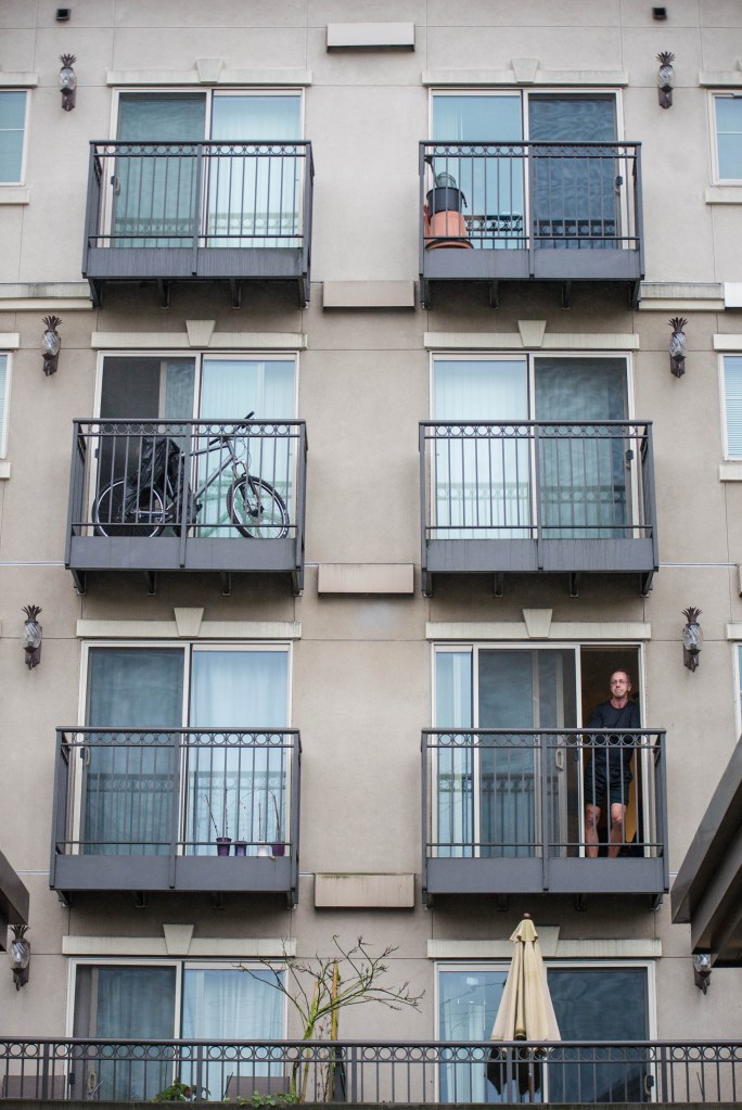 Residents of Onyx, an apartment building on the corner of East Olive Way and 12th Avenue, watch as protesters march back toward Cal Anderson Park in Capitol Hill, Saturday. Around one hundred people marched in honor of William Wingate's incident in which a Seattle police officer arrested Wingate claiming the golf club he used as a cane was a weapon on July 9, 2014.