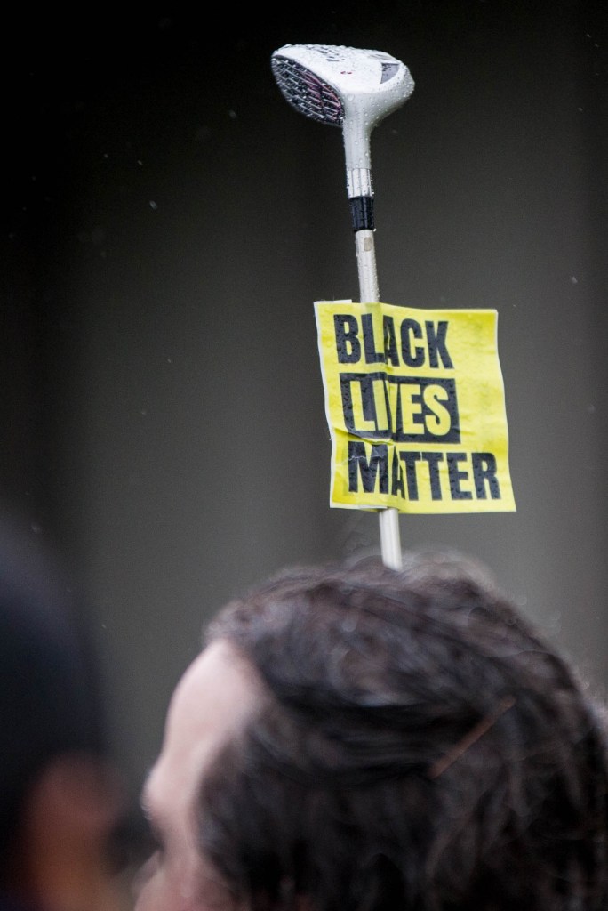 A woman holds a golf club with a "Black Lives Matter" sign during a Walking While Black: Always Dangerous Until Proven Otherwise protest on Capitol Hill Saturday, Feb. 7, 2015.