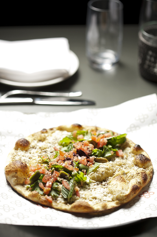The ma'noushe, recklessly splattered with briny white cheese; split green olives; cherry tomatoes (redder than they have a right to be in January); vibrant sprigs of parsley; and young olive oil. Underlying the garnishes is a base coat of za'atar, the salty, oiled elixir of dried thyme and toasted sesame seeds.