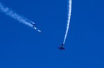Kirby Chambliss (pilot) flies barrel-rolls around the Red Bull Air Force (Skydivers) as they descend towards Genesee Park in wingsuits.