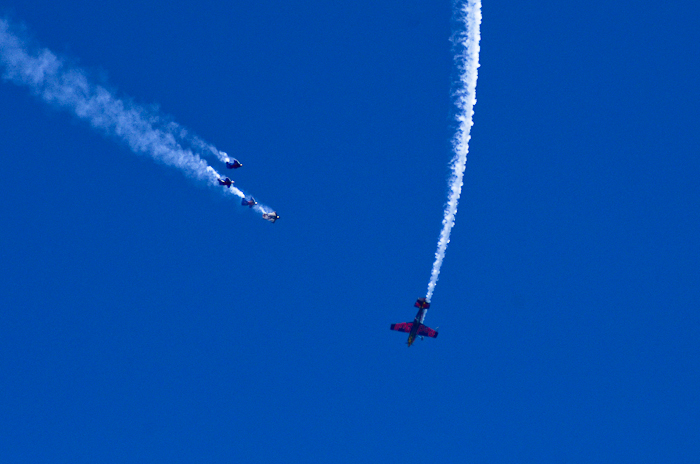 Kirby Chambliss (pilot) flies barrel-rolls around the Red Bull Air Force (Skydivers) as they descend towards Genesee Park in wingsuits.