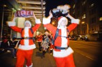 A pair of Santas carrying boomboxes down the street.