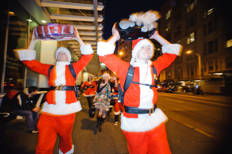 A pair of Santas carrying boomboxes down the street.