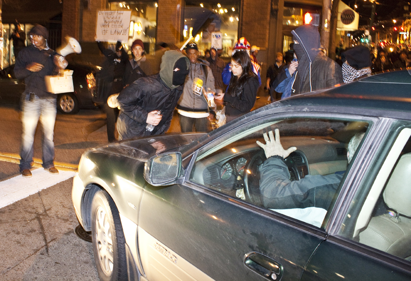 An Angry masked protester prevents this man from leaving the intersection, after several frustrating minutes he squeezes on by.