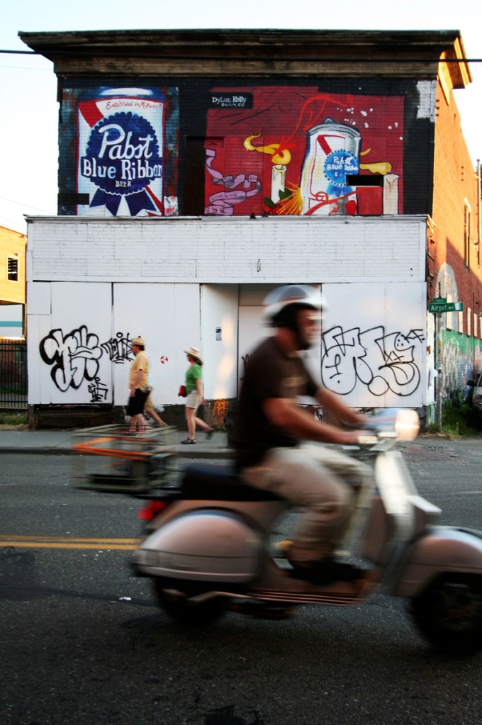 A moped speeds by a building decorated with Pabst Blue Ribbon in Georgetown during Artopia.