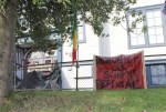A chain-link fence decorated in blood-red banners bearing messages like DECOLONIZE OUR