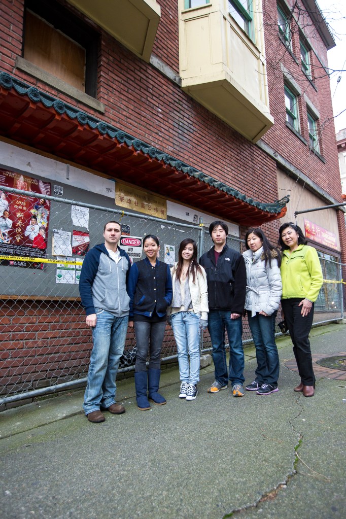 Members of the Woo family stand in front of the Community Billboard outside the fire-damaged Wah Mee building. Photo by Joshua Bessex