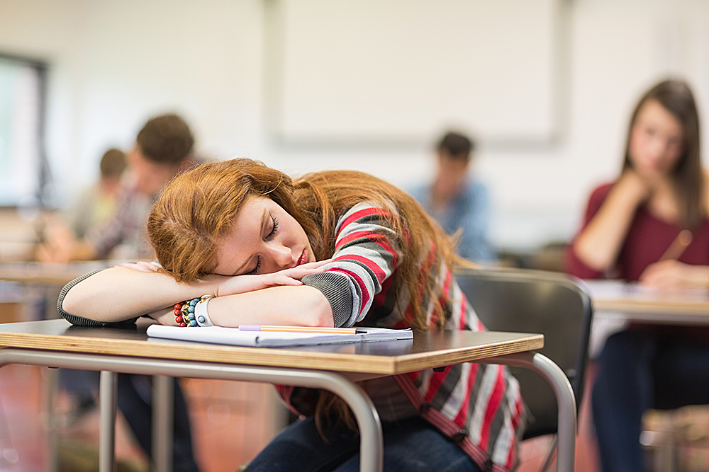 Blurred students in the classroom with one asleep girl