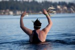 Dressed as Poseidon, a man weilds a trident as he walks slowly in over his head.