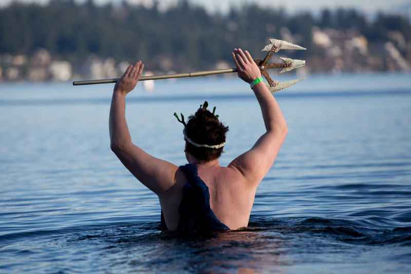 Dressed as Poseidon, a man weilds a trident as he walks slowly in over his head.