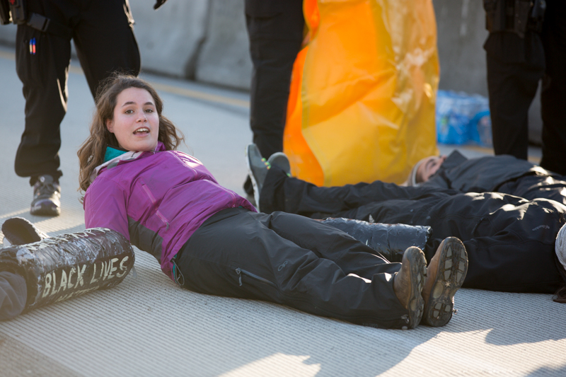 A protester glances at supporters on the sidewalk while lying in the middle of northbound SR-99.