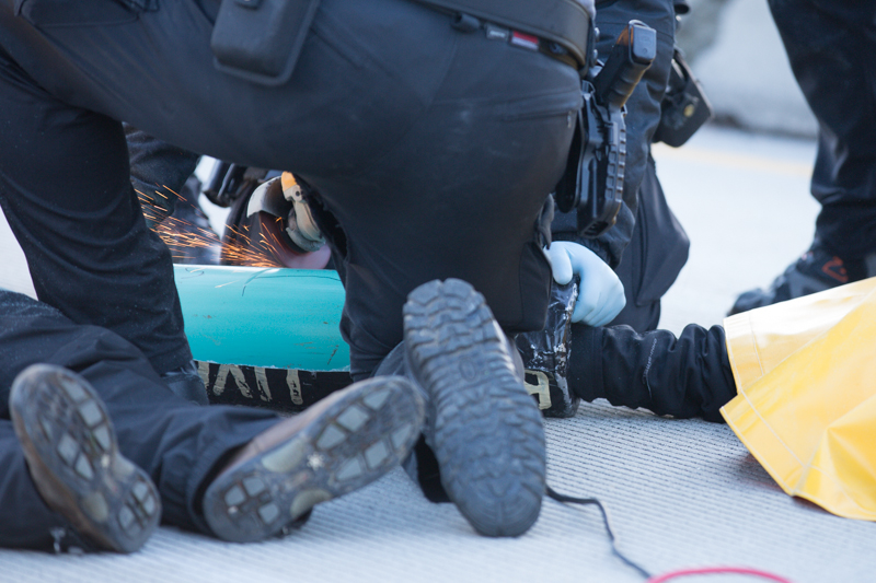 Police work to extricate protesters from PVC pipe devices locking them together.