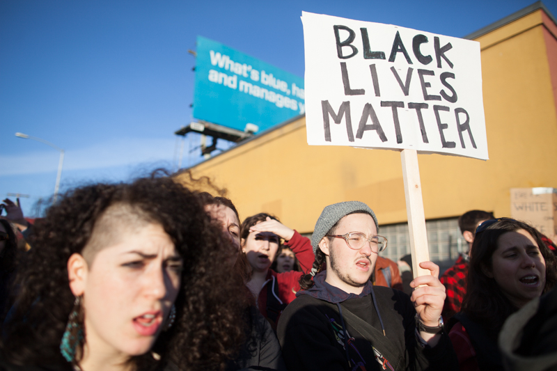 Supporters watch from the sidewalk.