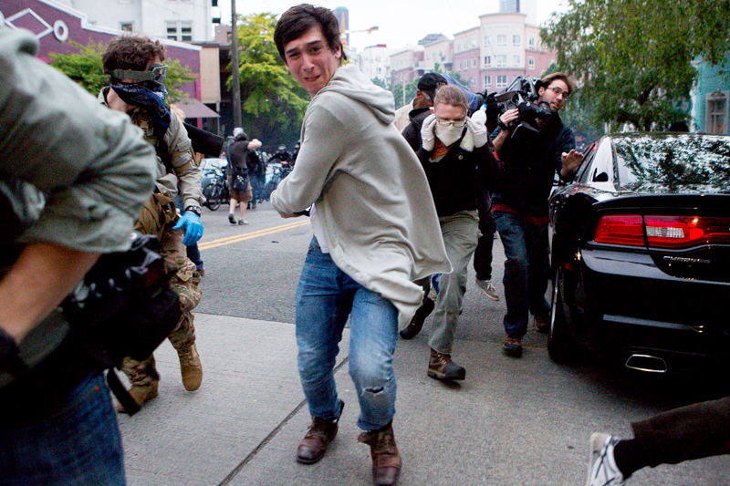 Protesters and media members run from a deployed flash bang grenade.