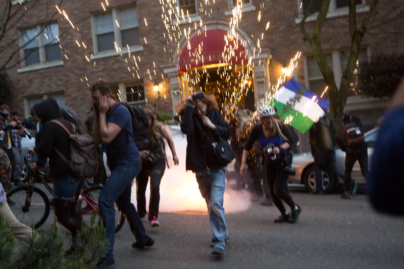 The percussive effects of a flash bang grenade jolt the camera as people run for cover.