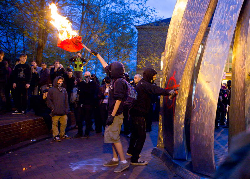 Protesters burn flags and mark a sculpture with graffitti on the Seattle Central campus.