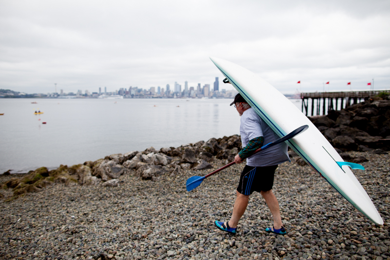 Paddleboard draped over his back, an activist makes his way to the beach to put into the water.