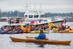 Kayaktivists line up for a waterborne demonstration as a Seattle police boat keeps watch.