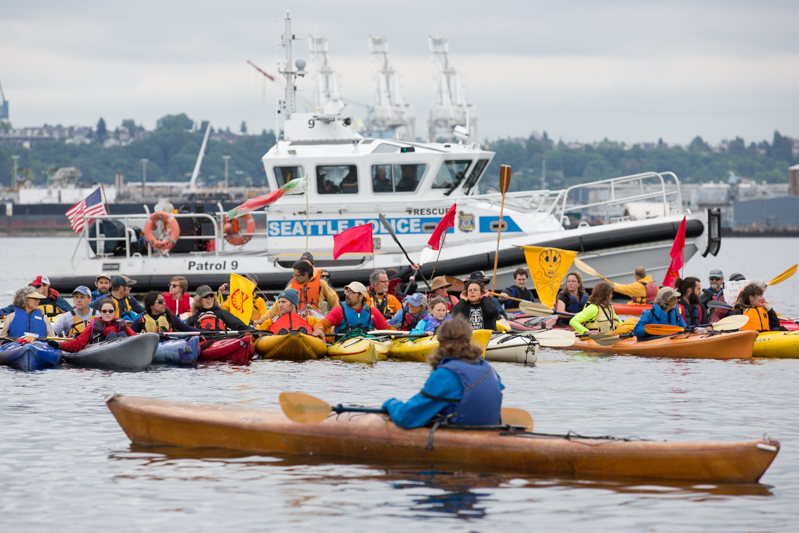 Kayaktivists line up for a waterborne demonstration as a Seattle police boat keeps watch.